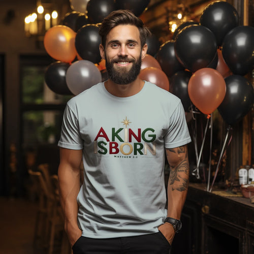 man wearing a light gray Christian Christmas T-shirt with 'A King Is Born' text, Bethlehem star, and Matthew 2:2.